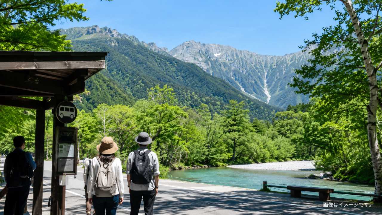 上高地の梓川と穂高連峰を背景に、手前にシャトルバス停と旅行者の後ろ姿